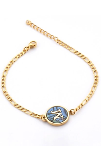 Detail of golden Figaro chain bracelet with a blue shell round pendant featuring letter M
