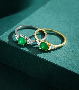 Detailed macro of S925 silver rings with emerald green stones on a dark textured background