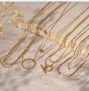 Macro detail of multi-layered 18K gold plated necklaces featuring OT buckle and ring charms
