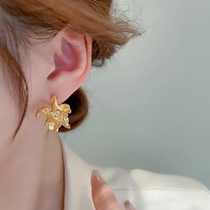 Detailed close-up of golden irregular pleated flower earrings on model with metal texture
