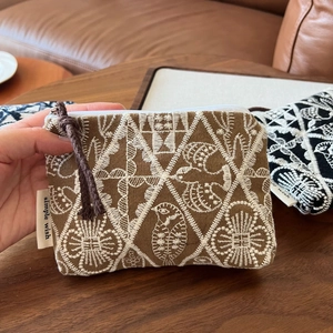 Close-up of cotton linen coin purse with floral embroidery and brand label on wood