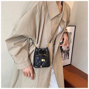 Detail of a quilted bucket bag featuring a camellia charm and gold chain strap