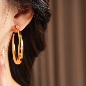 Close-up of gold C-shaped hoop earring with zircon detail worn by a model