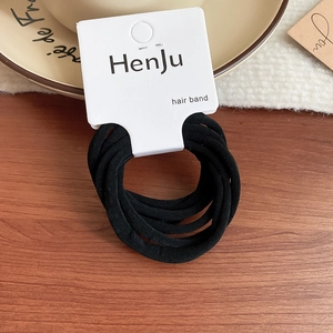 Detail of six black elastic hair bands on branded cardstock over wooden surface
