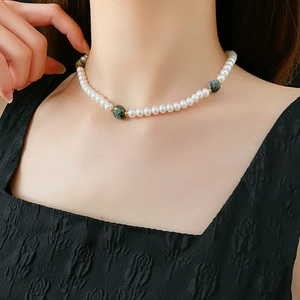 Détail du collier de perles avec accents de pierres précieuses vertes et billes dorées