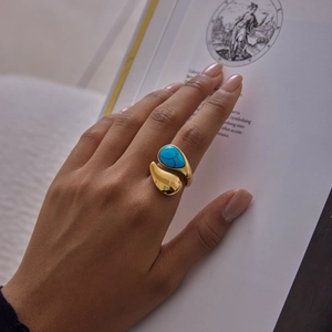 Detail of a gold-plated teardrop blue stone ring worn by a model in a vintage setting