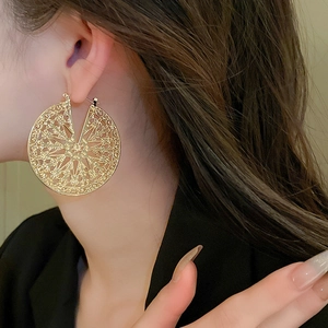 Gros plan de boucles d'oreilles dorées avec motif floral évidé porté par un mannequin