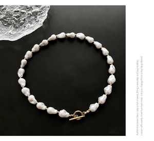 Detail of irregular white baroque pearl necklace with golden metal toggle clasp