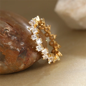 Macro shot of gold eternity ring featuring square-cut zircon stones on textured rock