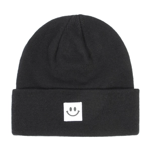 Close-up of black knitted beanie featuring a white square patch with a grey smiley face