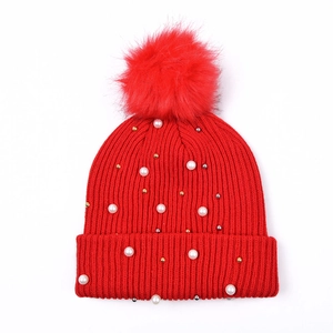 Dettaglio cappello in maglia rossa con pompon, perle bianche e perline metalliche
