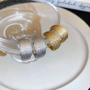Detail shot of gold and silver textured hoop earrings hanging on a glass rim