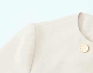 Dettaglio del tessuto beige di un blazer con bottone decorativo in metallo dorato