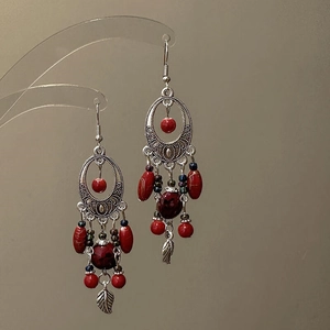 Detail of bohemian tassel earring with silver hollow metal frame and red beads