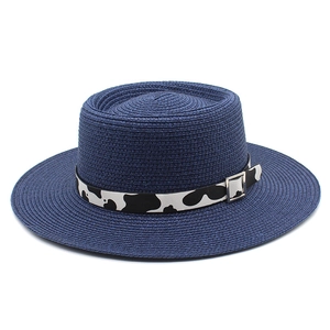 Detail of navy blue woven straw hat featuring cow print band and metal buckle strap
