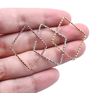 Three textured 18k gold and silver diamond shaped pendant charms held in hand for scale