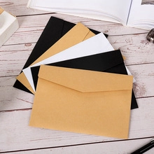 Close-up of kraft, black, and white paper envelopes arranged on a wooden desk surface
