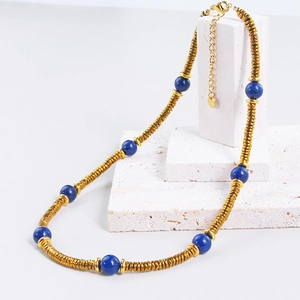 Detail of beaded necklace with gold metal tubes and deep blue stones on stone background