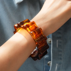 Dettaglio del bracciale in acrilico ambra con bordi ondulati sul polso di una modella