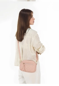 Pink quilted crossbody camera bag with adjustable strap shown on model for scale