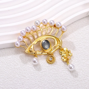 Golden Evil Eye brooch with pearls and grey gemstone on minimalist textured background