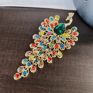 Detailed macro view of the rhinestone-encrusted peacock brooch with a large green pear-cut gem