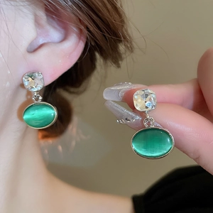Detailed view of silver dangle earrings featuring green cat eye stone and square crystal