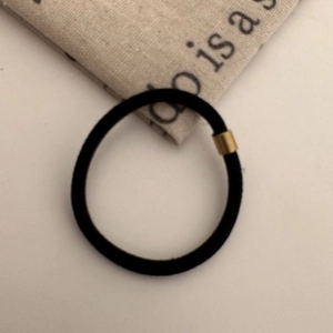 Detail of a high-elastic black hair tie with a decorative gold metal buckle on a neutral fabric