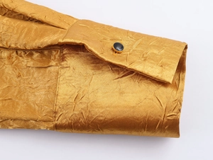 Detailopname van een satijngouden jurkmouw met geplooide textuur en een zwarte knoop