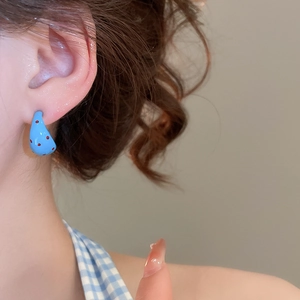 Close-up of blue C-shaped drop earrings with red polka dots worn by a model