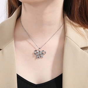Close-up of a silver hollow bow pendant necklace worn on a model's neck for a trendy look