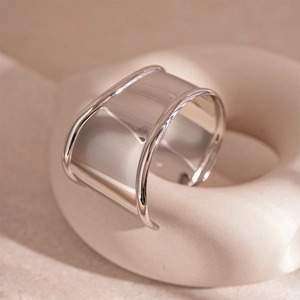 Detailed view of wide silver geometric ring with polished finish on beige wavy stand