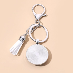 Silver metal keychain with white tassel and round pendant on orange background