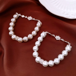 Detailed macro of white pearl bracelets with zircon flower pendants on silk