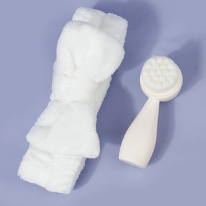 White plush bow headband and soft bristle facial cleansing brush set on purple background