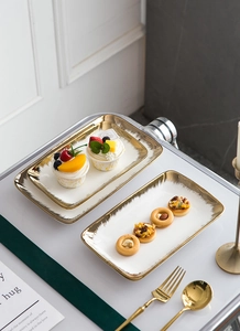 Close-up of elegant rectangular ceramic plates with gold rims on a marble table