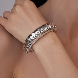 Macro shot of silver metal bangle with irregular rippled texture on a woman's wrist
