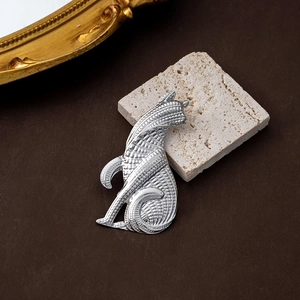 Detail view of a vintage silver cat brooch with textured relief on a rustic stone base