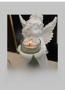 Close-up of white angel figurine holding a glass candle holder with burning tea light