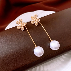 Close-up of 18k gold-plated pearl flower earrings on a textured brown leather display