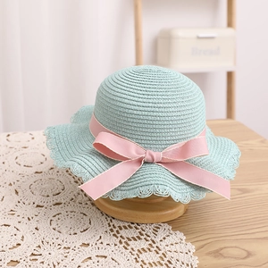 Détail d'un chapeau de paille vert menthe avec nœud rose et bord en dentelle évidé