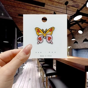 Close-up of a colorful butterfly enamel pin with pink hearts on a white display card