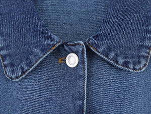 Macro detail of denim jacket collar with silver metal buttons and brown contrast stitching