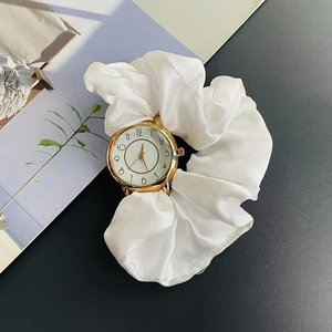 Detailed close-up of a gold-tone quartz watch with a white silk scrunchie wristband strap