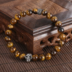 Detailed view of men's tiger eye bead bracelet with silver skull charm on wooden base