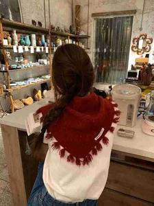 Detail shot of a red knitted triangle scarf with tassel fringe worn in a cozy indoor setting