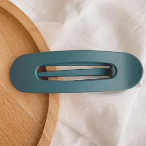 Close-up of matte dark teal oval cutout hair clip on a natural wooden tray background