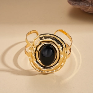 Detail of a wide gold cuff bracelet featuring hammered texture and a black oval gemstone