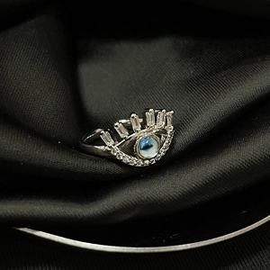 Macro shot of silver eye-shaped ring with blue zircon center on black silk fabric