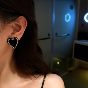 Retro black heart earrings with gold trim on model under cinematic blue neon lighting